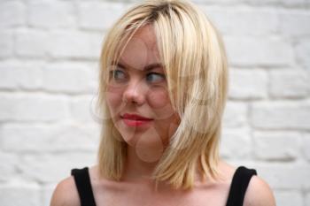 A stunningly beautiful young blond woman with bright blue eyes against wall