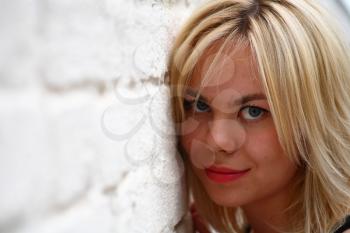 A stunningly beautiful young blond woman with bright blue eyes against wall