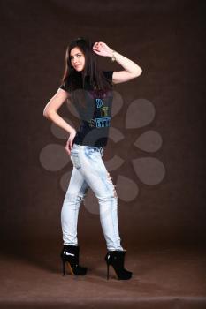 beautiful young blond girl in jeans poses perfect on brown