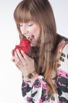 Beautiful young woman eating red heart. Isolated over white background.