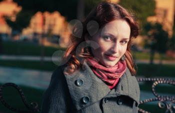 Red haired young female head and shoulders shot outside in autumn park, weared bright red scarf and coat. She looking at camera and smiling. Toned image.