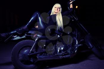 Young sexy fashionable blond haired lady lying on motorcycle bike in the night misty blue background