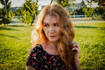 young redhead woman sitting on bench in park looking away the camera in calm state of mind.