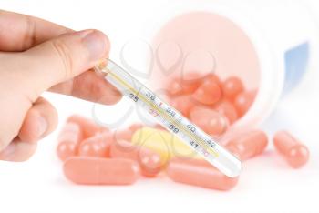 Human Hand with thermometer on pills background. Sickness concept.