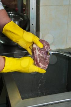 Hands in gloves washing and cleaning meat at the kitchen sink