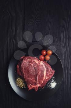 Fresh raw beef meat steaks in the black plate with spices on black wooden background