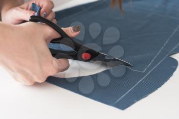 Woman dressmaker cutting fabric textile with scissors