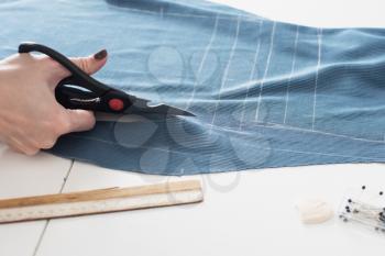 Woman dressmaker cutting fabric textile with scissors