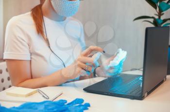 Woman disinfects the surface of the phone by sanitizer spray on the working place. Coronavirus concept. Woman in quarantine for coronavirus covid-19 working from home.