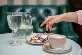 Closeup photo of female hands is reaching out to cake with cup of coffee in restaurant