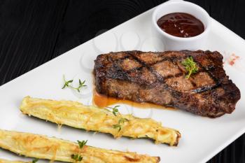 Grilled black angus strip loin steak New York with zucchini on white plate on black wooden background with