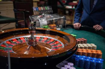 Casino, gambling and entertainment concept - roulette table and stack of poker chips