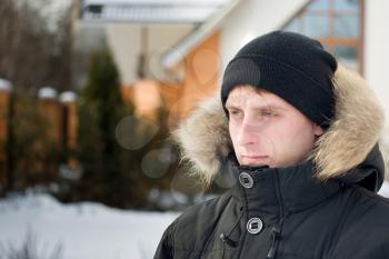 Winter holidays - man in cap and warm jacket with furry hood in the yard