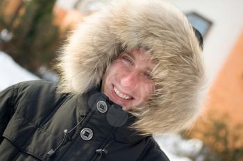 Winter time - smiling man in warm jacket with furry hood in the yard