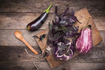 Aubergines, basil and spoon on chopping board and wooden table. Rustic style and autumn food photo