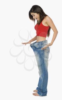 Woman pulling jeans from waistline to show weight loss and looking shocked