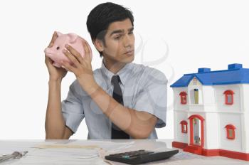 Real estate agent holding a piggy bank near his ear