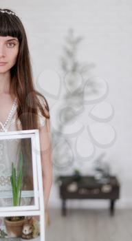 Photo of a young girl in the style of fine art, her hand is holding a large glass florarium inside which are plants and a bunny figure.