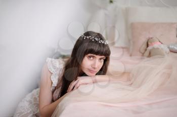 Photo of a young girl in the style of fine art. Close-up portrait of a girl with a diadem in her hair that rests with her hands on a beautiful romantic bed.