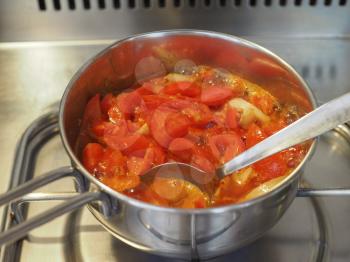 tomato soup preparation boiling in a sauce pan on gas cooker with spoon