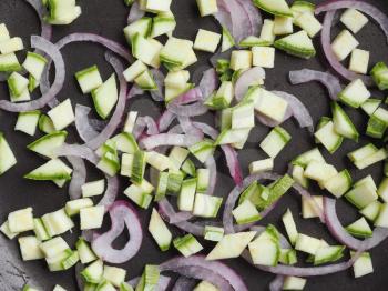 raw vegetables in a frying pan including red onions rings and courgettes