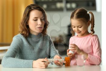 Young woman and daughter with pills at table�