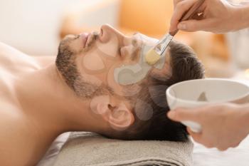Cosmetologist applying cosmetic mask on man's face in spa salon�
