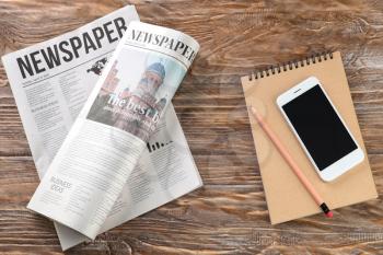 Morning newspapers and mobile phone on wooden table�