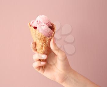 Woman holding waffle cone with delicious strawberry ice-cream on color background�