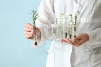 Laboratory worker holding test tubes with plants on color background, closeup�