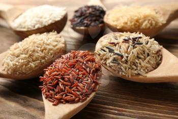 Different types of rice in spoons on wooden background�