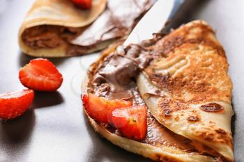 Tasty thin pancakes with chocolate spread and strawberries on plate, closeup�