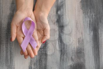 Woman holding lavender ribbon on wooden background. Cancer awareness concept�