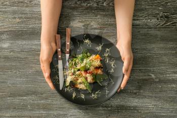 Woman holding plate with healthy fresh salad on wooden background�