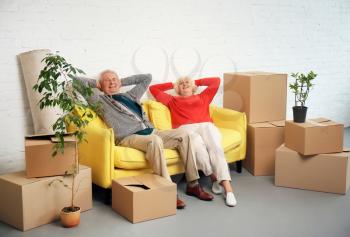 Mature couple sitting on sofa near boxes after moving into new house�