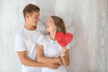 Happy young couple with red heart near grey wall�