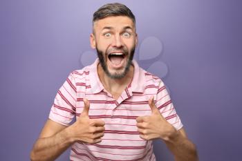 Happy man showing thumb-ups gesture on color background�