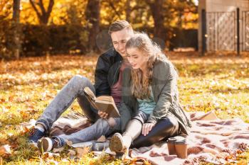 Loving young couple reading book on plaid in autumn park�