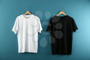 Hangers with blank t-shirts on color background�