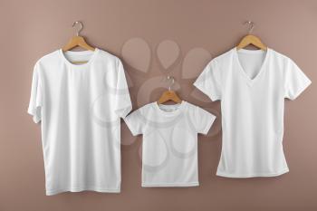 Hangers with blank white t-shirts on color background�