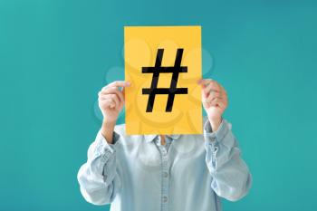 Woman holding sheet of paper with hashtag sign on color background�