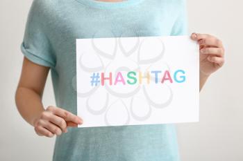 Woman holding sheet of paper with hashtag on light background�