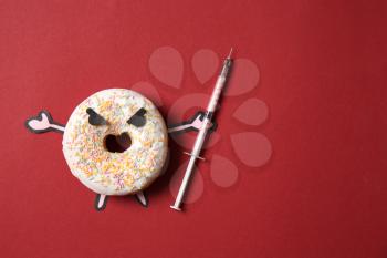 Angry doughnut with syringe on color background. Concept of addiction�