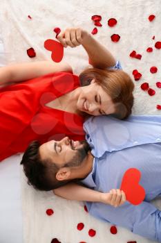 Happy young couple with red hearts lying on bed at home. Celebration of Saint Valentine's Day�