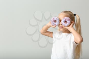 Cute little girl with donuts on light background�