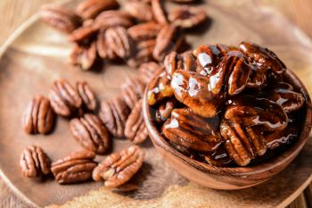 Bowl with tasty candied pecan nuts on wooden plate�