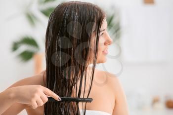Young woman combing beautiful long hair in bathroom�