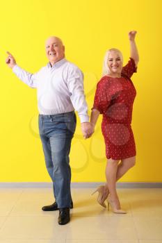 Cute elderly couple dancing near color wall�