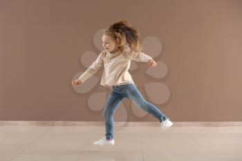 Active little girl jumping against color wall�