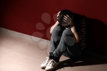 Young depressed woman thinking about suicide near wall�